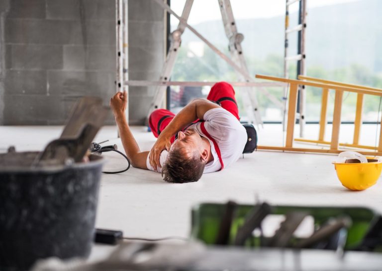 A construction worker lying on the ground holding his shoulder after a building site accident.