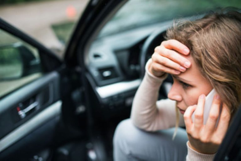 A woman sitting in her car, on the phone, looking concerned after a car accident