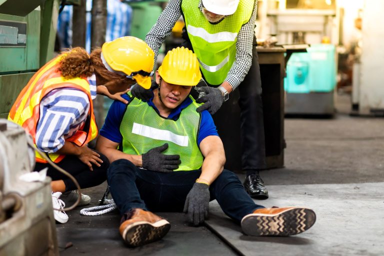 Staff in high vis and hard hats helping a colleague after an accident at work