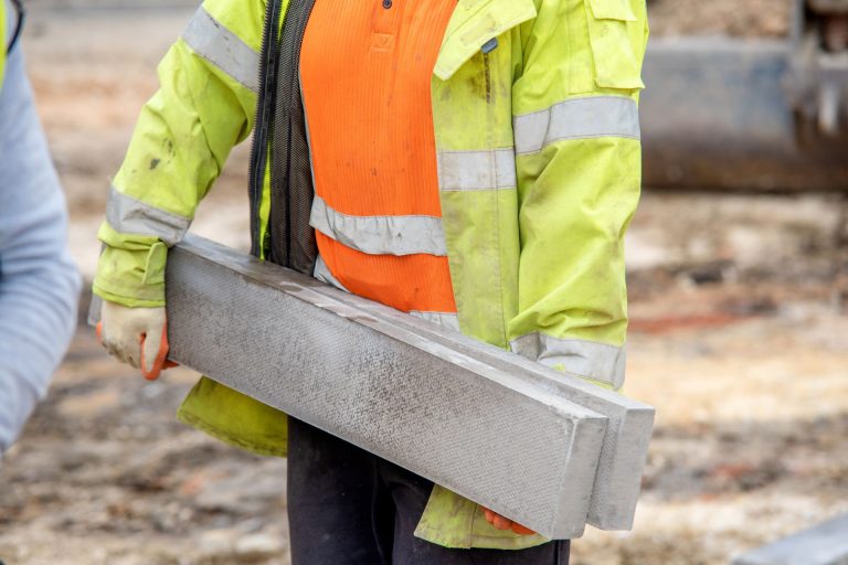A construction worker in high vis carrying a concrete curb